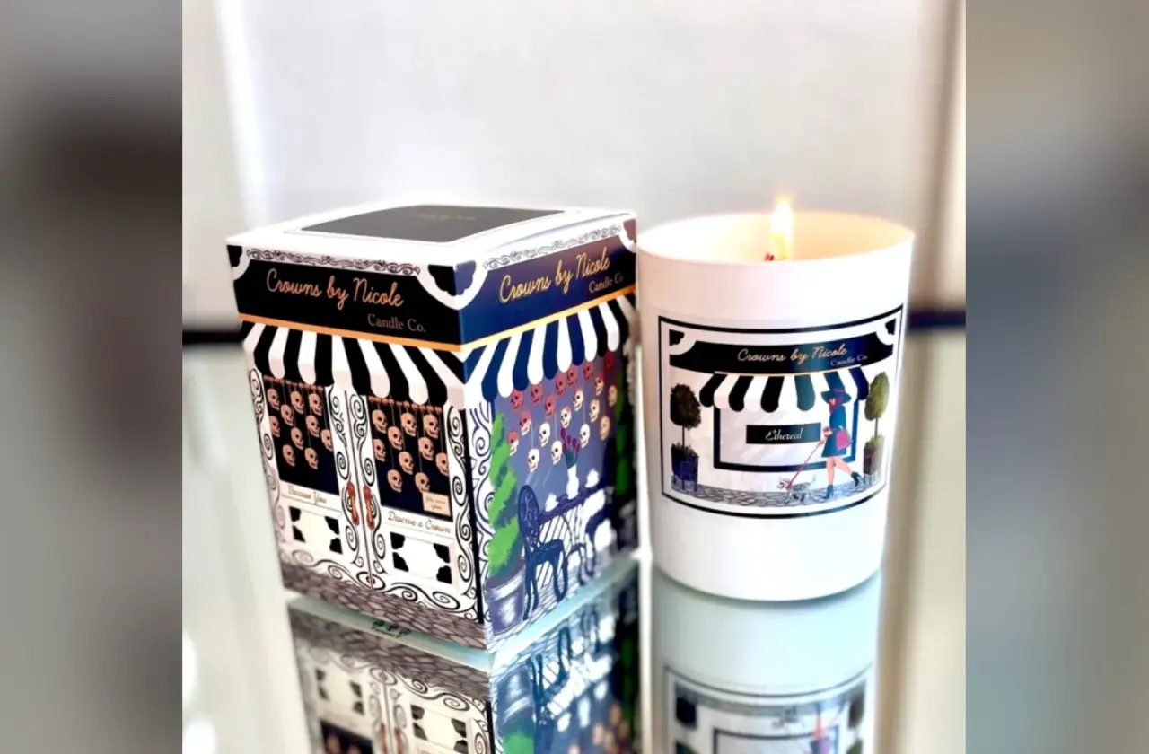 A lit scented candle next to its decorative packaging featuring whimsical black and white designs.
