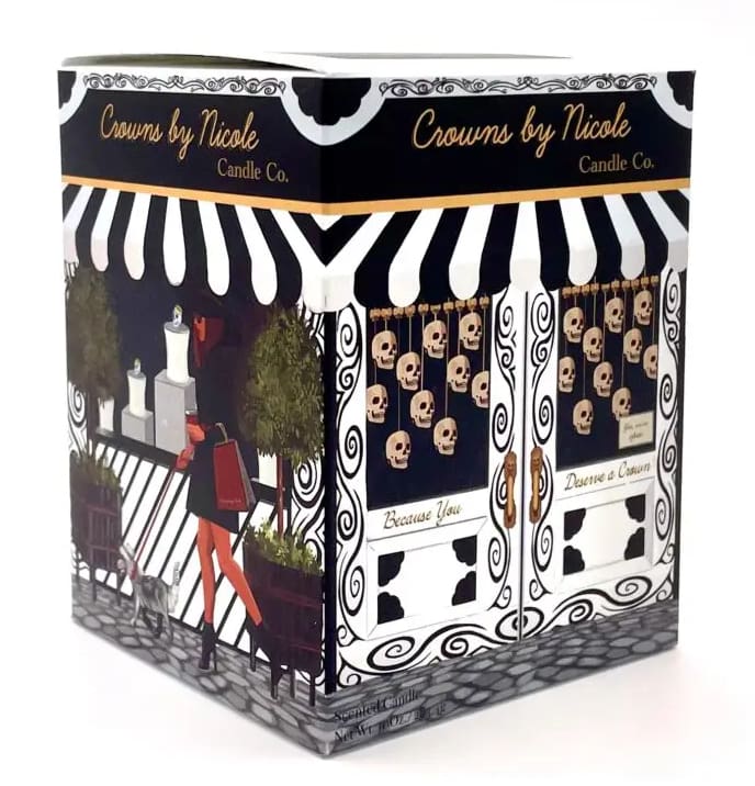 Decorative candle packaging featuring a black and white skull motif with an illustrated scene of a person at a fence, labeled "crowns by nicole candle co.