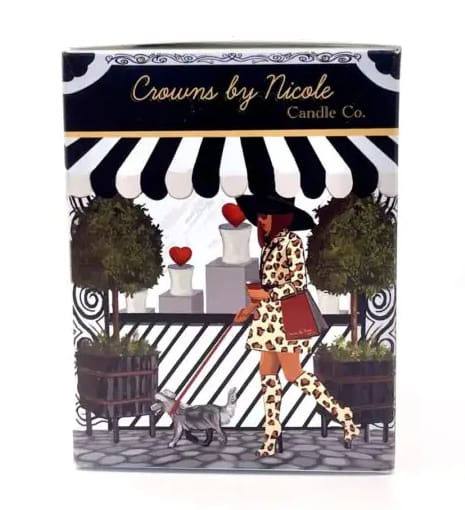 A decorative candle box featuring a stylized illustration of a woman in a fashionable outfit walking a dog under an awning labeled "crowns by nicole candle co.